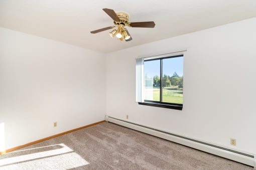 an empty living room with a ceiling fan and a window. Hutchinson, MN Deer Park Apartments