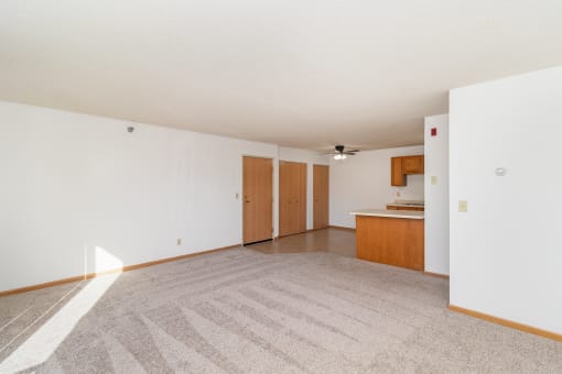 an empty living room and kitchen with white walls and carpet. Hutchinson, MN Deer Park Apartments