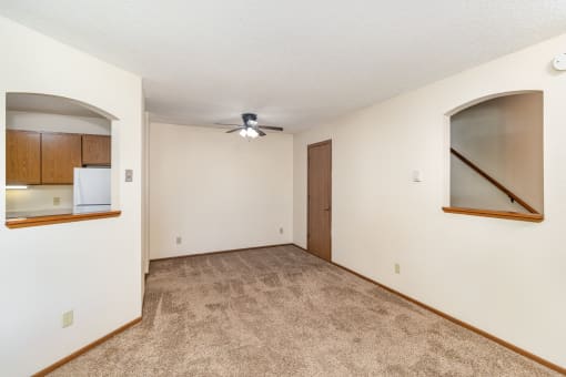 an empty living room with a ceiling fan and a door to a kitchen. Hutchinson, MN Twin Oaks Townhomes