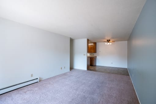 the living room and dining room of an apartment with carpet and white walls. Fargo, ND Betty Ann Apartments