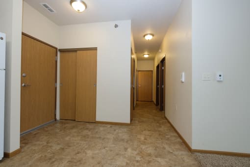 a hallway with white walls and wooden doors and a carpeted floor. Fargo, ND North Sky Apartments