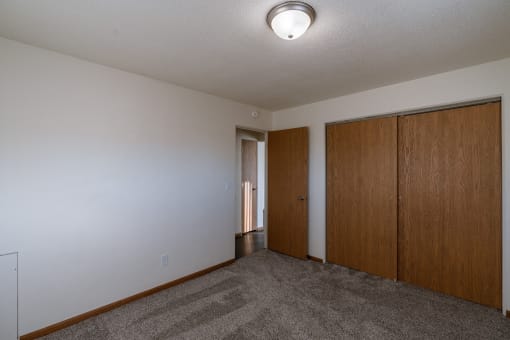 an empty living room with a carpeted floor and two wooden doors. Fargo, ND North Manor Apartments