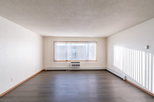 an empty living room with a large window and wood floors. Fargo, ND North Manor Apartments