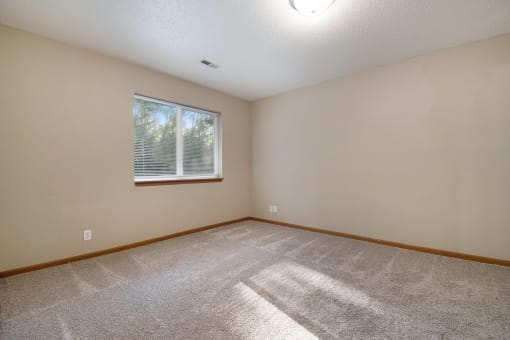 Omaha, NE Deerfield Apartments. An empty bedroom with a large window and beige walls