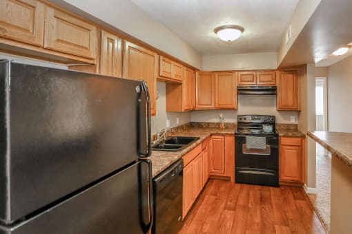 a kitchen with wooden cabinets and appliances and a black refrigerator. Omaha, NE Evergreen Terrace Apartments