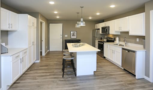A kitchen with white cabinets and a wooden floor. Fargo, ND 29 West Apartments