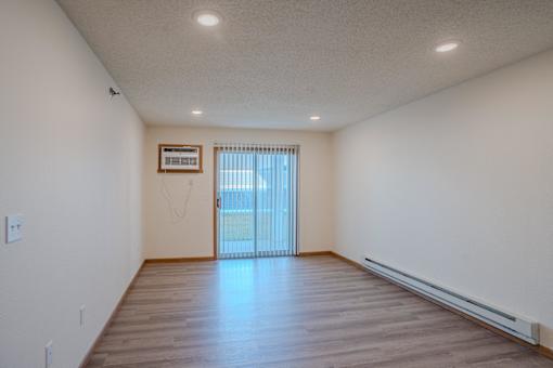 an empty living room with wood floors and a sliding glass door. Fargo, ND Lake Crest Apartments