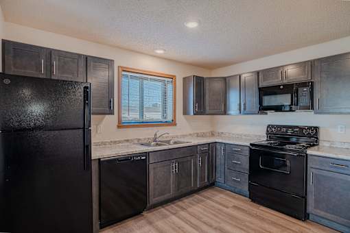 a kitchen with black appliances and wood flooring. Fargo, ND Lake Crest Apartments