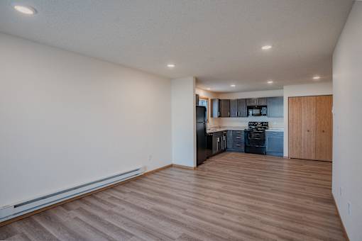 an empty living room and kitchen with wood floors and white walls. Fargo, ND Lake Crest Apartments