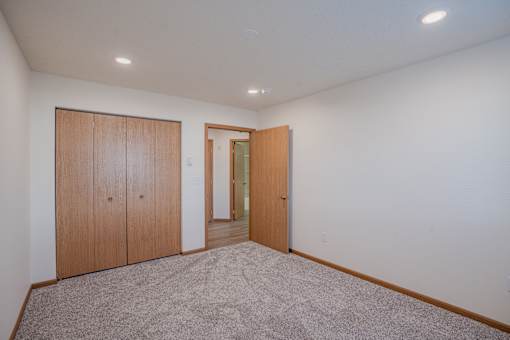 a living room with carpet and a door to a hallway. Fargo, ND Lake Crest Apartments