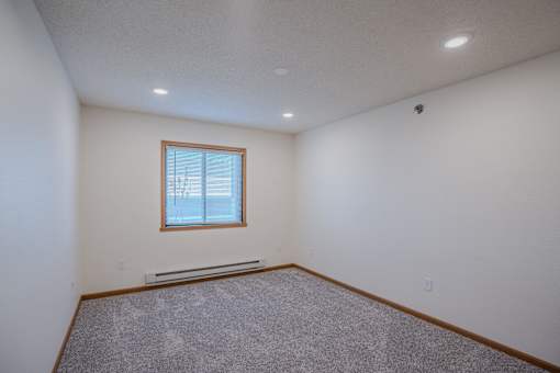 an empty living room with carpet and a window. Fargo, ND Lake Crest Apartments
