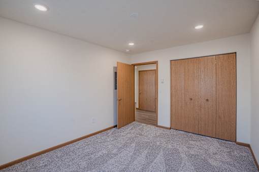 a living room with a carpeted floor and a door to a hallway. Fargo, ND Lake Crest Apartments
