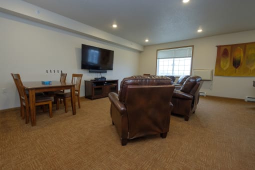 an open community room with leather furniture and a television. Fargo, ND North Sky Apartments