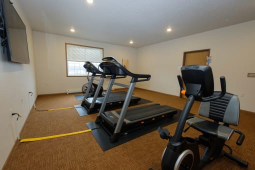 a fitness room with two treadmills and a tv. Fargo, ND North Sky Apartments