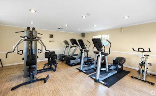 A gym with a variety of equipment including treadmills, stationary bikes, and weight machines. at The Oaks Apartments, Upland