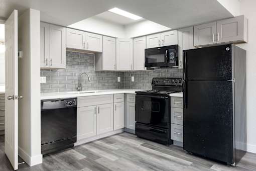 A black refrigerator stands in a kitchen with white cabinets and a black oven.