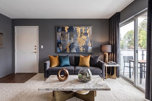 A modern living room with a grey couch, a large abstract painting, and a marble coffee table.