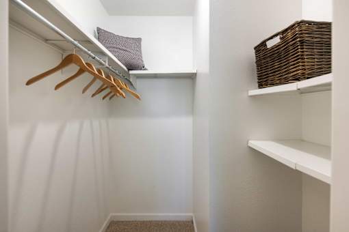 a walk in closet with white walls and shelves and wooden hangers