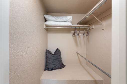 a walk in closet with pillows and a bag on a shelf in a closet
