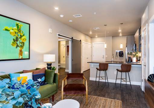 A living room with a green couch and a painting of yellow flowers on the wall.