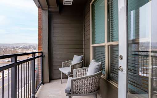 Two chairs are on a balcony with a view of the city.