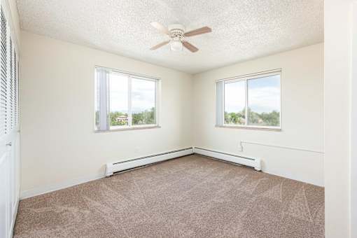 an empty bedroom with a ceiling fan and two windows