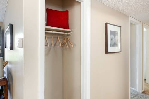a closet with a red pillow and a white shelf with hangers