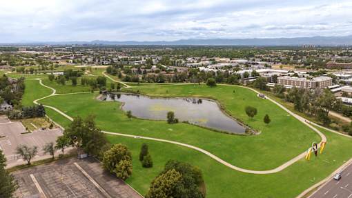 an aerial view of a park with a pond and a city in the background