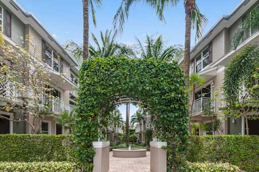 the archway of an apartment complex with palm trees and greenery