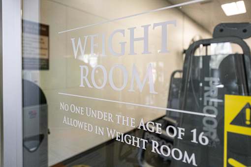 a weight room sign on the door of a gym with escalators