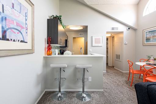 a bar with three stools in a living room with a kitchen and a hallway