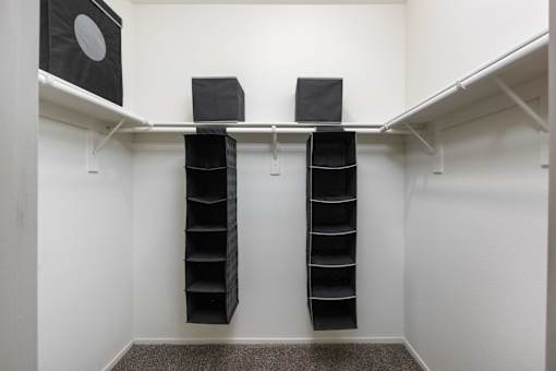 a walk in closet with black shoe racks and a white wall