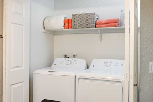 a white washer and dryer in a white laundry room with a shelf above