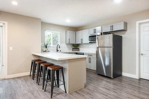 a kitchen with a large island with bar stools and a stainless steel refrigerator