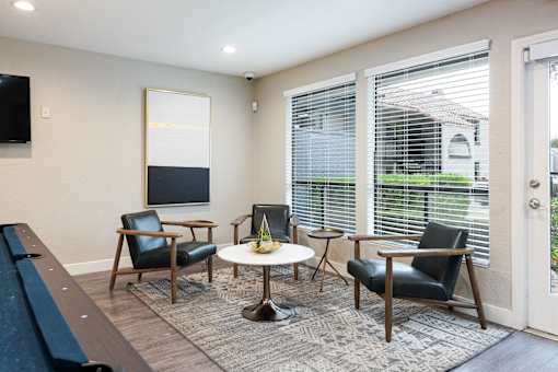 a living room with chairs and a table and large windows
