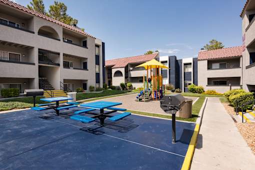 an outdoor play area with picnic tables and an umbrella
