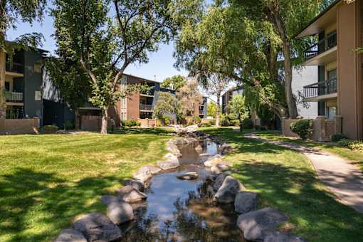 a stream runs through a grassy area between two apartment buildings