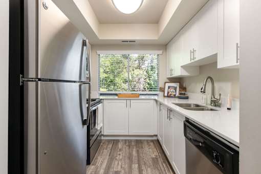 a white kitchen with stainless steel appliances and a window