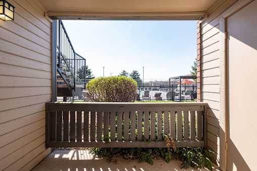 a balcony with a wooden bench and a view of a building and a playground