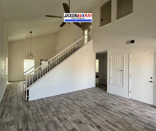 A spacious room with wooden flooring and a staircase leading to the upper level.