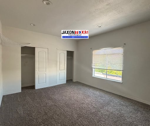 A room with a carpeted floor and a window with blinds.
