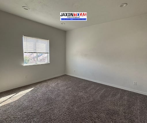 A room with a carpeted floor and a window letting in sunlight.