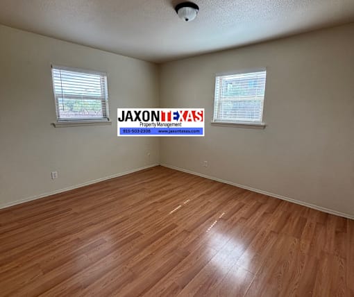 A room with wooden flooring and a JAXON PROPERTY MANAGEMENT sign on the wall.
