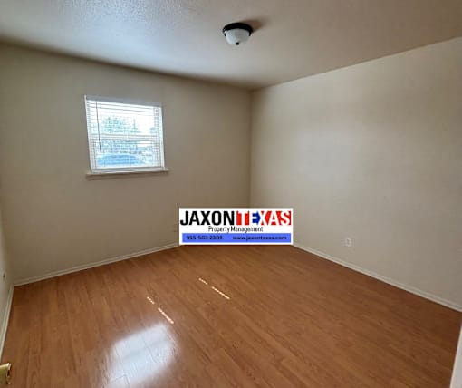 A room with wooden flooring and a window with a view of a building outside.