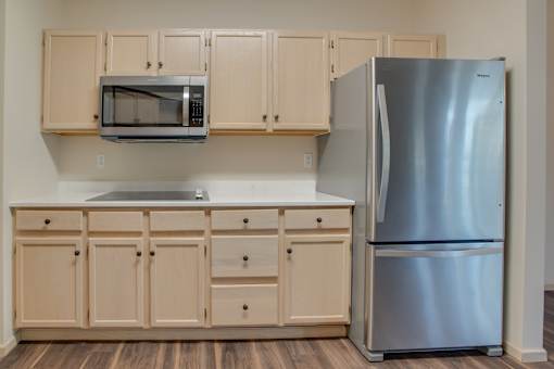 A kitchen with a stainless steel refrigerator and wooden cabinets. at Eighth Street Manor  Apartments, Fargo, ND