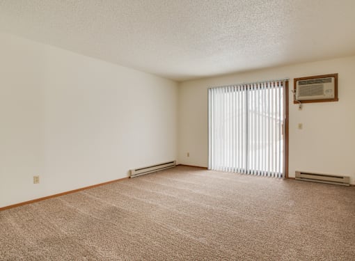 A room with a carpeted floor and a window with blinds.