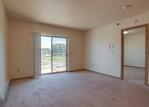 A room with a carpeted floor, a sliding glass door, and a mirror on the wall, Kassenborg Apartments, Moorhead, MN, 56560