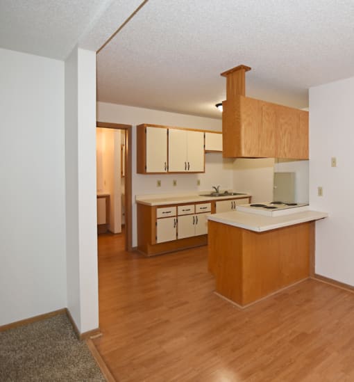 an empty kitchen and living room with wood flooring and wooden cabinets at Aspen Apartments, Hudson, WI, 54016