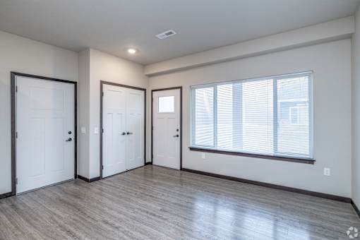 A room with a window, wooden floors, and white walls.