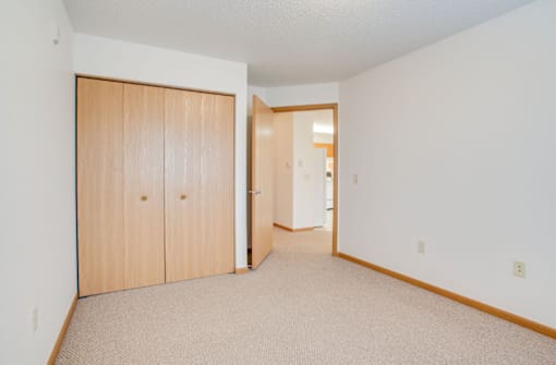 A room with a tan carpet and two wooden doors. at Savanna Apartments, St Cloud, 56303
